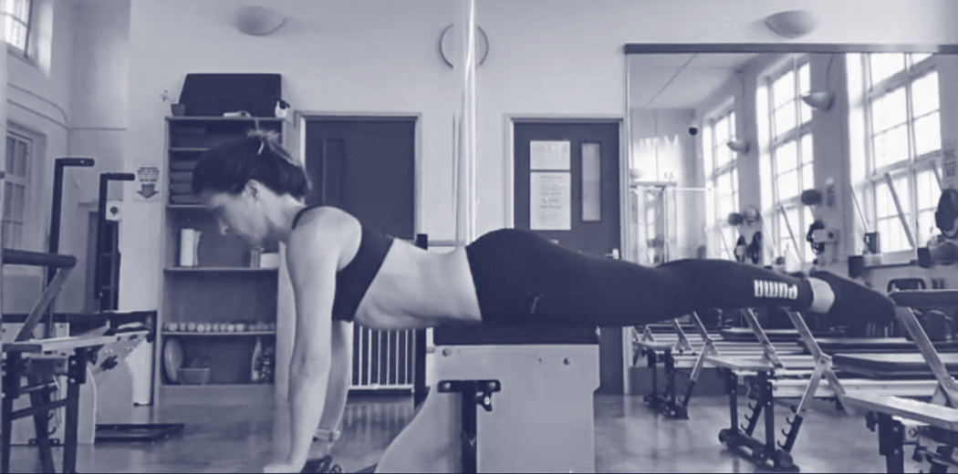 A person is performing an exercise on a Pilates reformer machine in a workout studio.